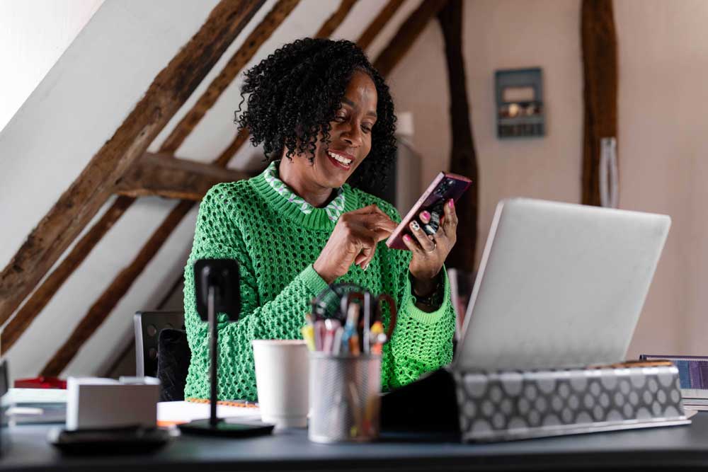 woman looking at her phone at desk with computer
