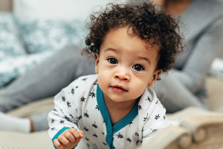 An infant in a onesie looks curiously at the camera.