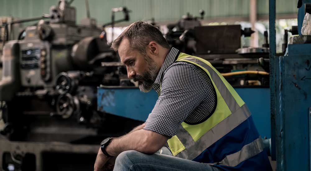 man in vest in factor looking sad