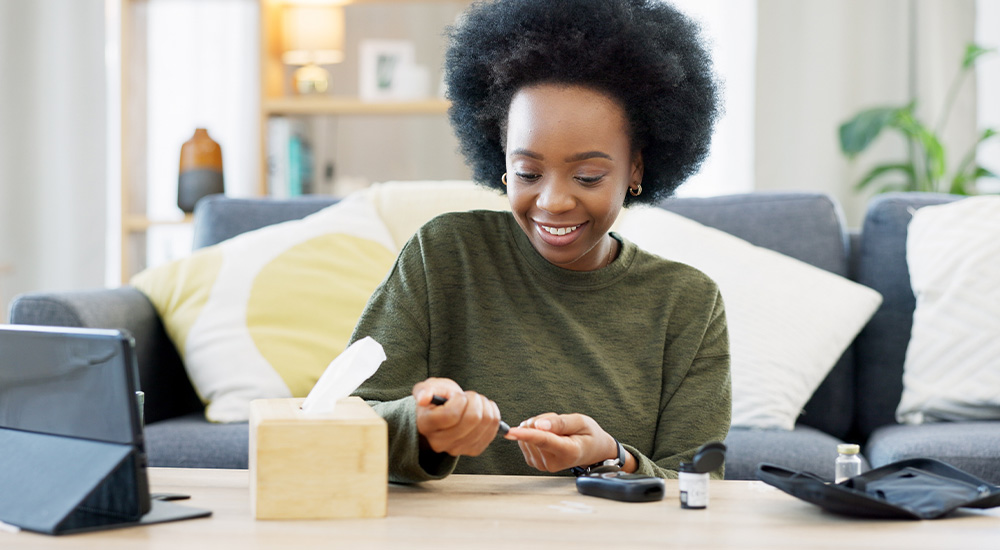 A woman sits on a couch with her laptop open, beside a box of tissues, appearing focused and engaged in her work.
