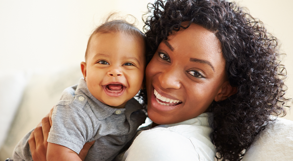 A joyful woman smiles while cradling a baby in her arms, radiating warmth and love.